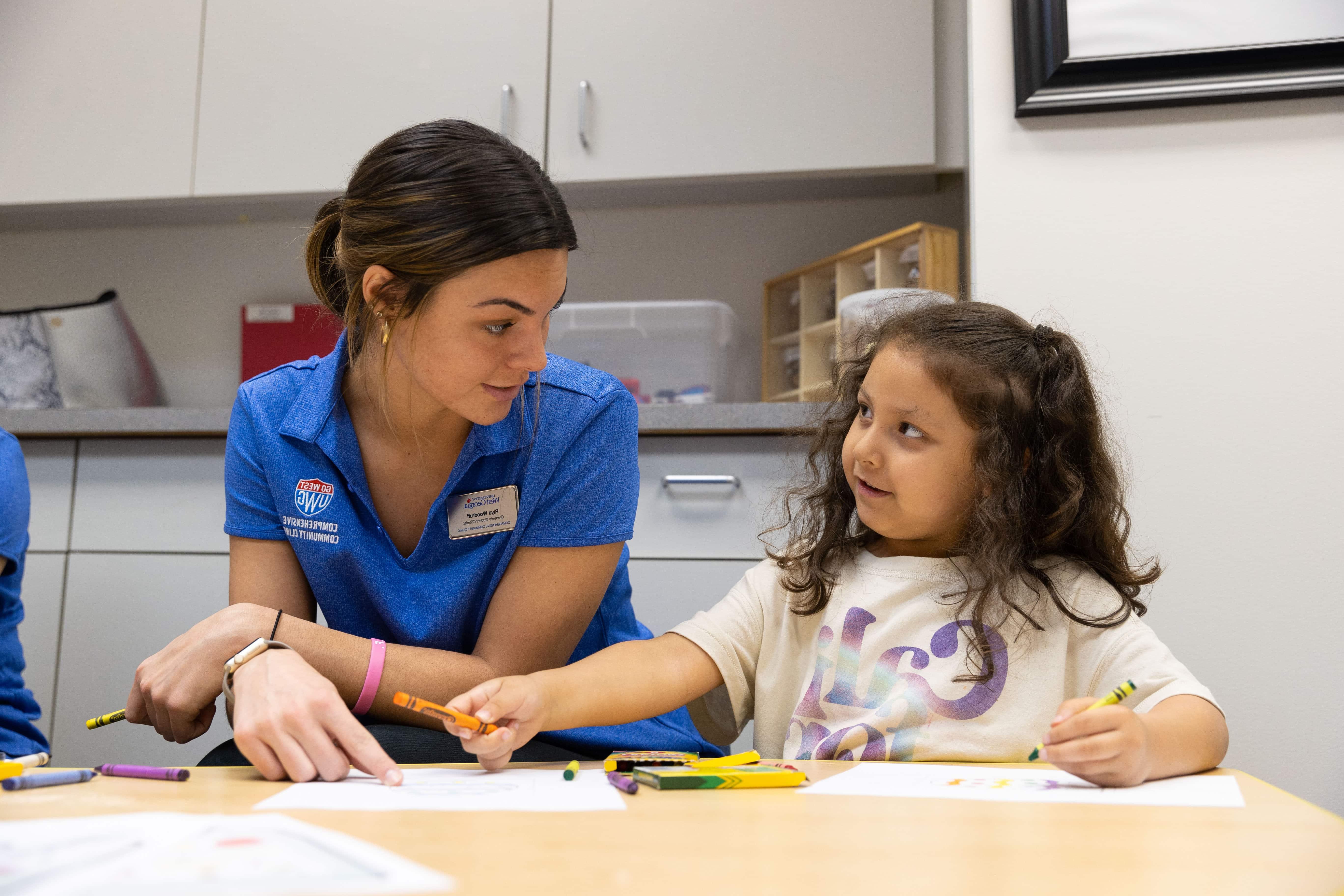 Early Learning Center teacher sitting with student using crayons.